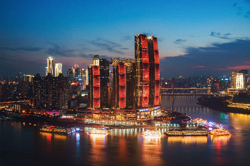 Vista nocturna de los rascacielos iluminados y barcos en el río de Chongqing
